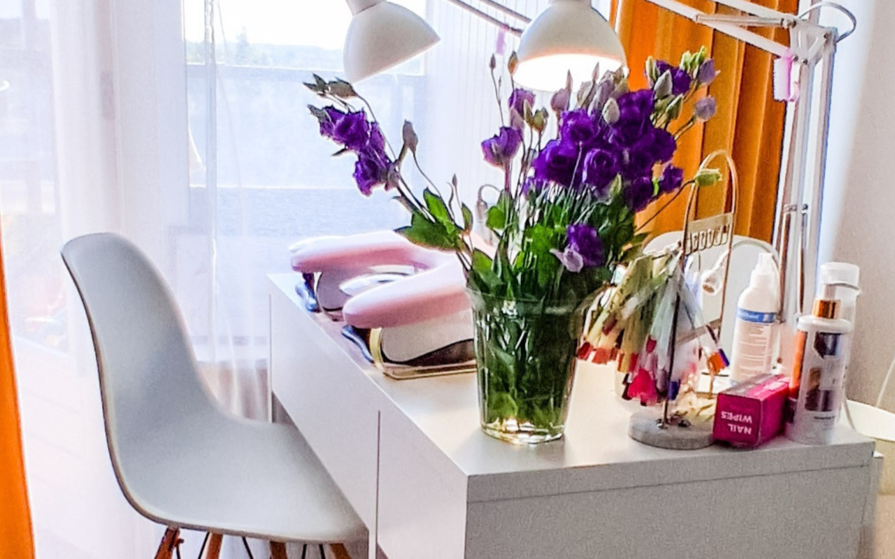 De werktafel in de studio met paarse bloemen, een lamp en een witte stoel