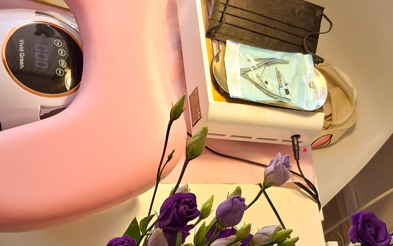 Roze nagellamp, gereedschap en paarse bloemen op de werktafel